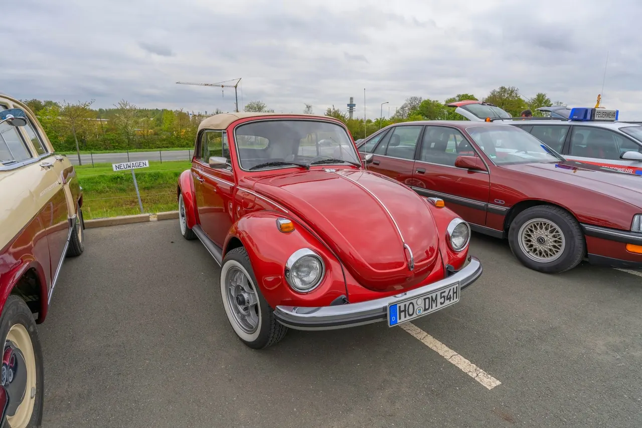 A polished classic car on a lawn display, bonnet open, with an owner standing beside the front wing.